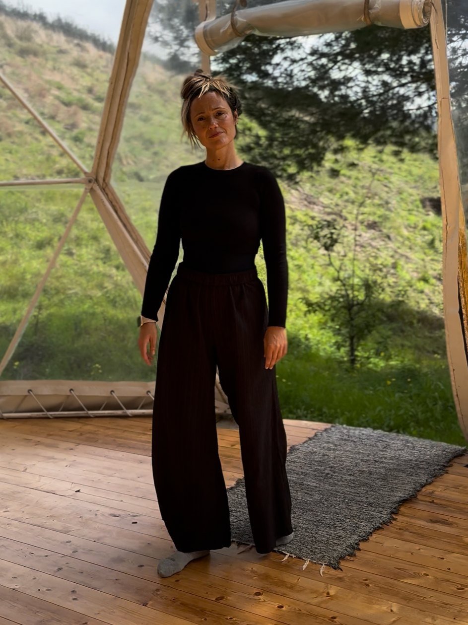 Mulher de pé, serena, num domo de madeira com vista para a serra